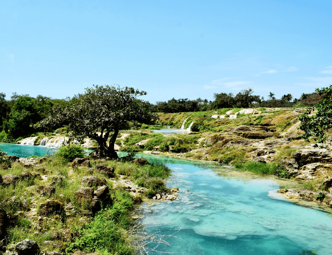 Salalah in Oman A Wadi in Jebel Samhan near Salalah - blue clear water surrounded by lush green scenery and blue sky