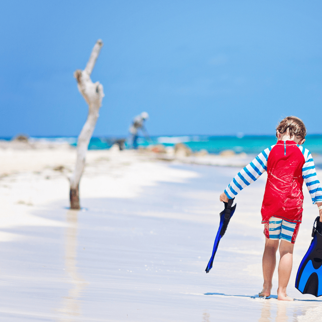 FamilyMaldivesBeachKid Little boy walking along a beach in the Maldives holding diving flippers.