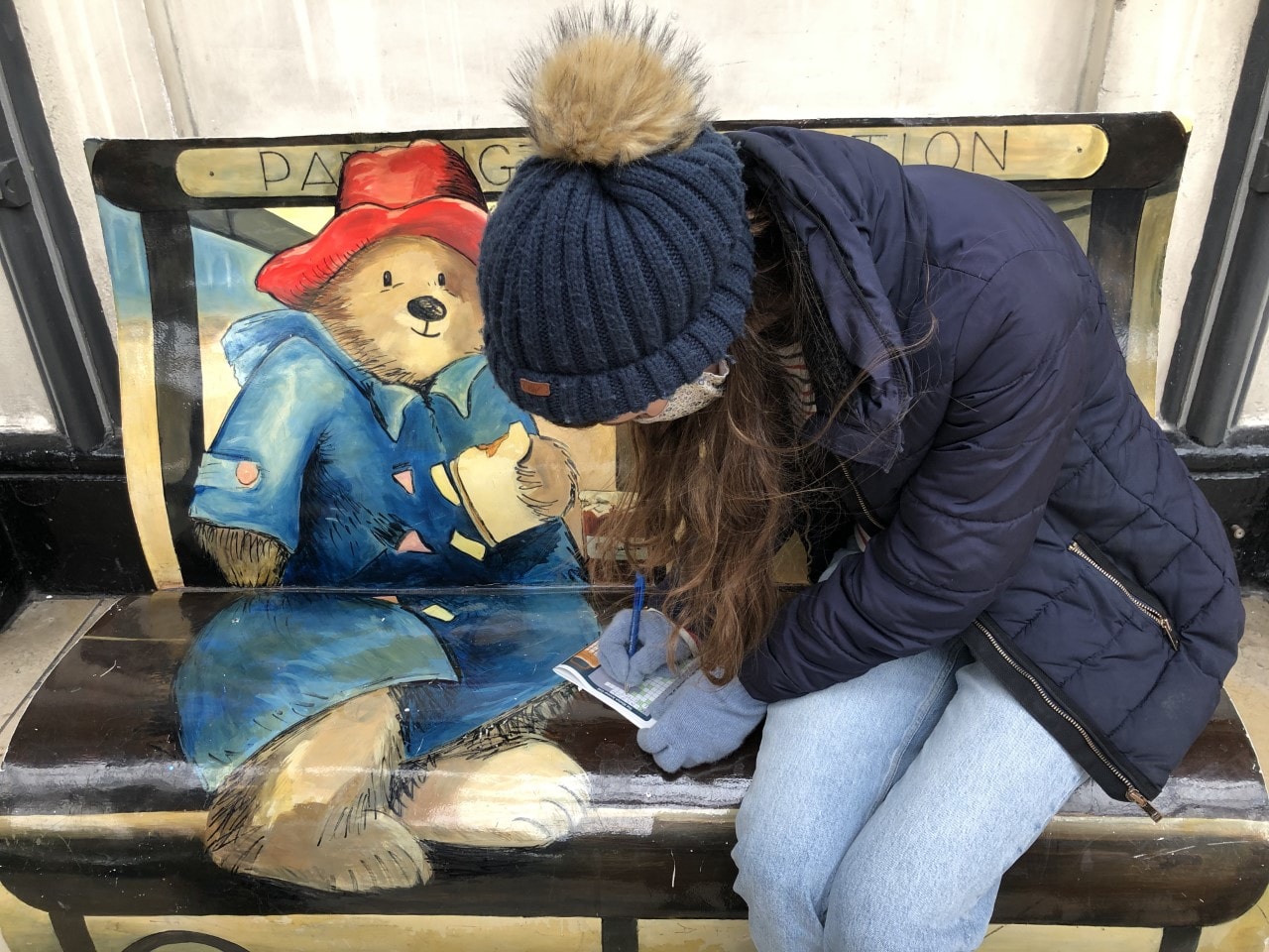 Treasure Trail in Paddington, London Woman completing a treasure trail map on a paddington bear bench in London