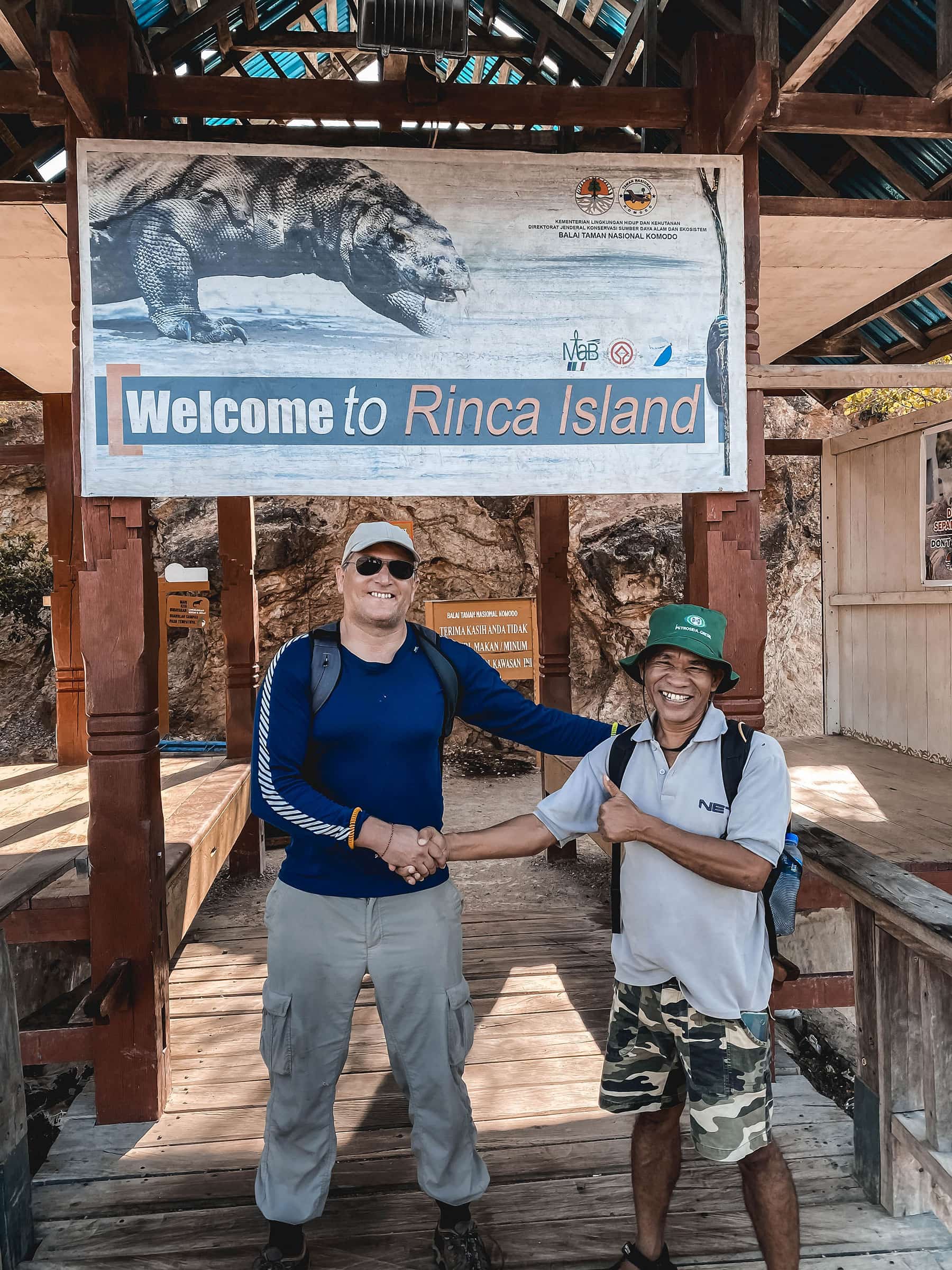 Rinca-Island Traveller shaking hands with a guide on wooden walkway under a sign for rinca island