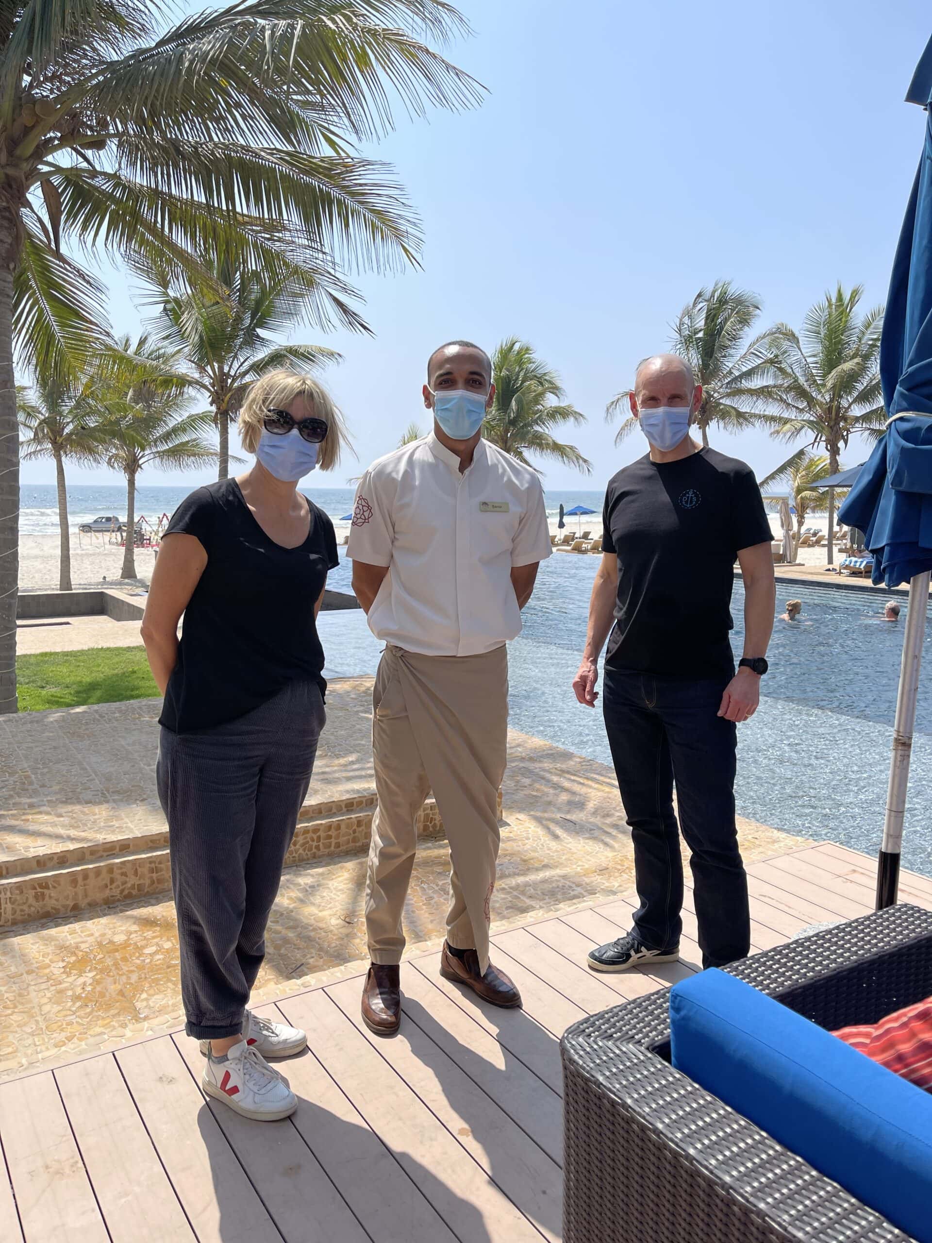 Lynne and Andy in Salalah travellers and hotel general manager wearing masks with beach in the background