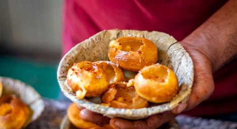 A person holding a bowl of Puchkas an Indian hollow snack A person holding a bowl of Puchkas an Indian hollow snack