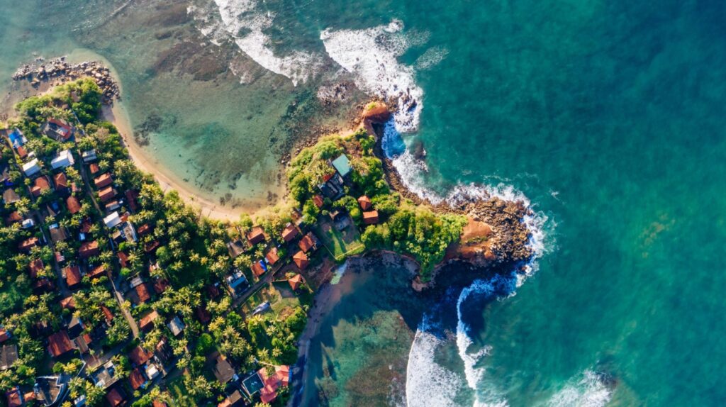 Aerial shot of a coastal Sri Lankan town with waves hitting the shore Aerial shot of a coastal Sri Lankan town with waves hitting the shore