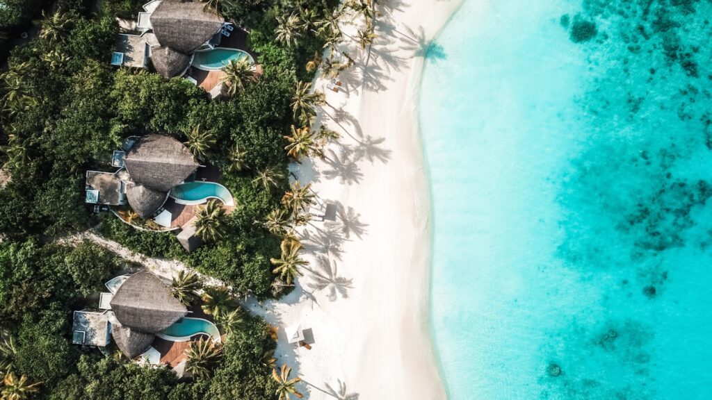 Aerial shot of Villas with private swimming pools leading to white sand and turquoise water Aerial shot of Villas with private swimming pools leading to white sand and turquoise water
