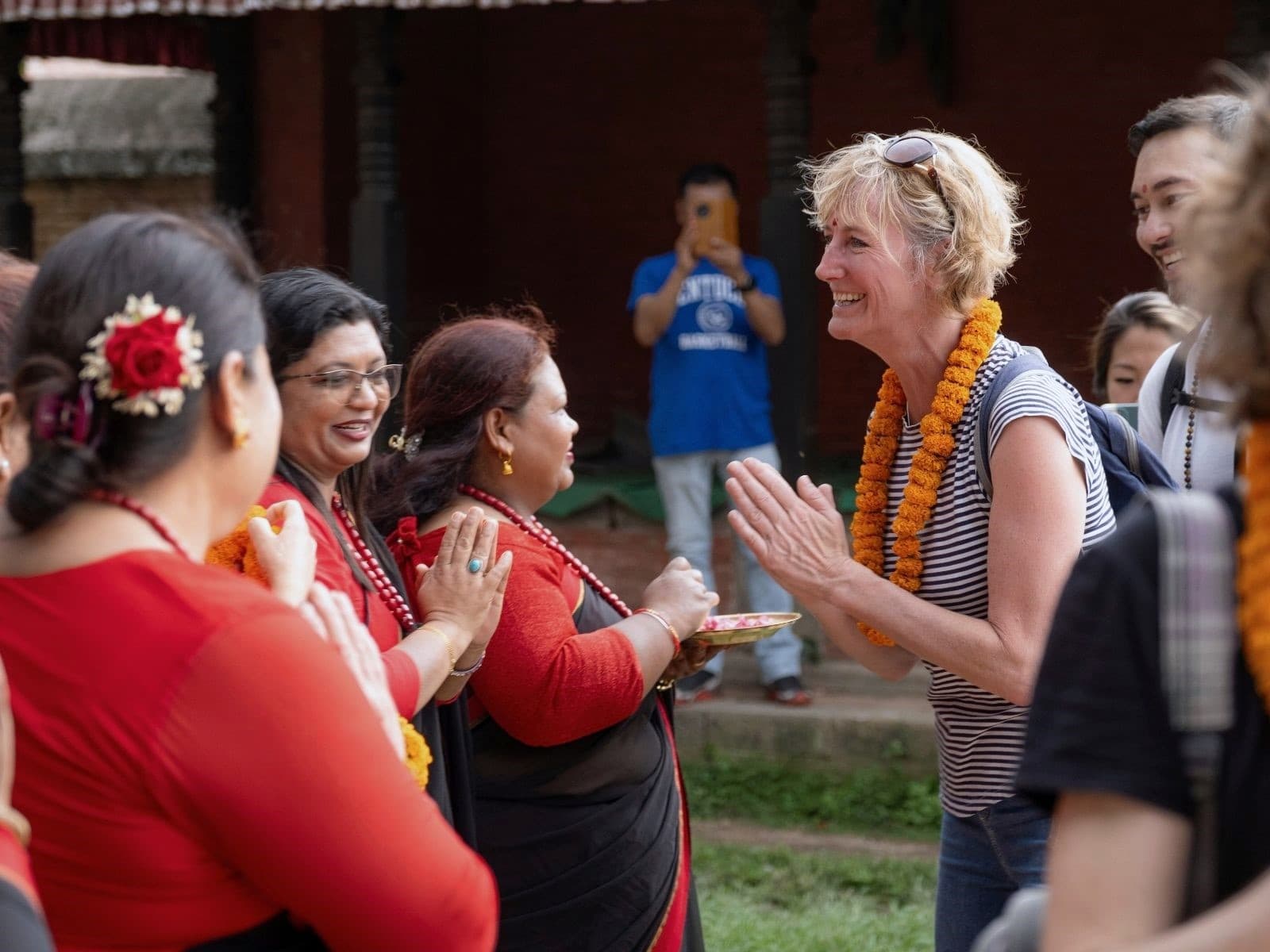 Sara Wells receives a warm traditional welcome with garlands and greetings from Nepalese women in red attire.